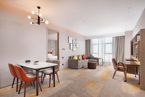 A modern hotel room with a dining area, a sofa, and a TV.