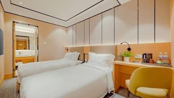 Une chambre d’hôtel avec deux lits, un bureau, une chaise et une salle de bain visible à travers une porte ouverte.