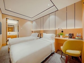 Habitación de hotel con dos camas, un escritorio, una silla y un baño visible a través de una puerta abierta.