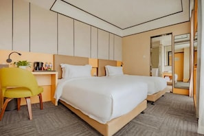 Habitación de hotel con cama doble, escritorio con silla, espejo y planta.