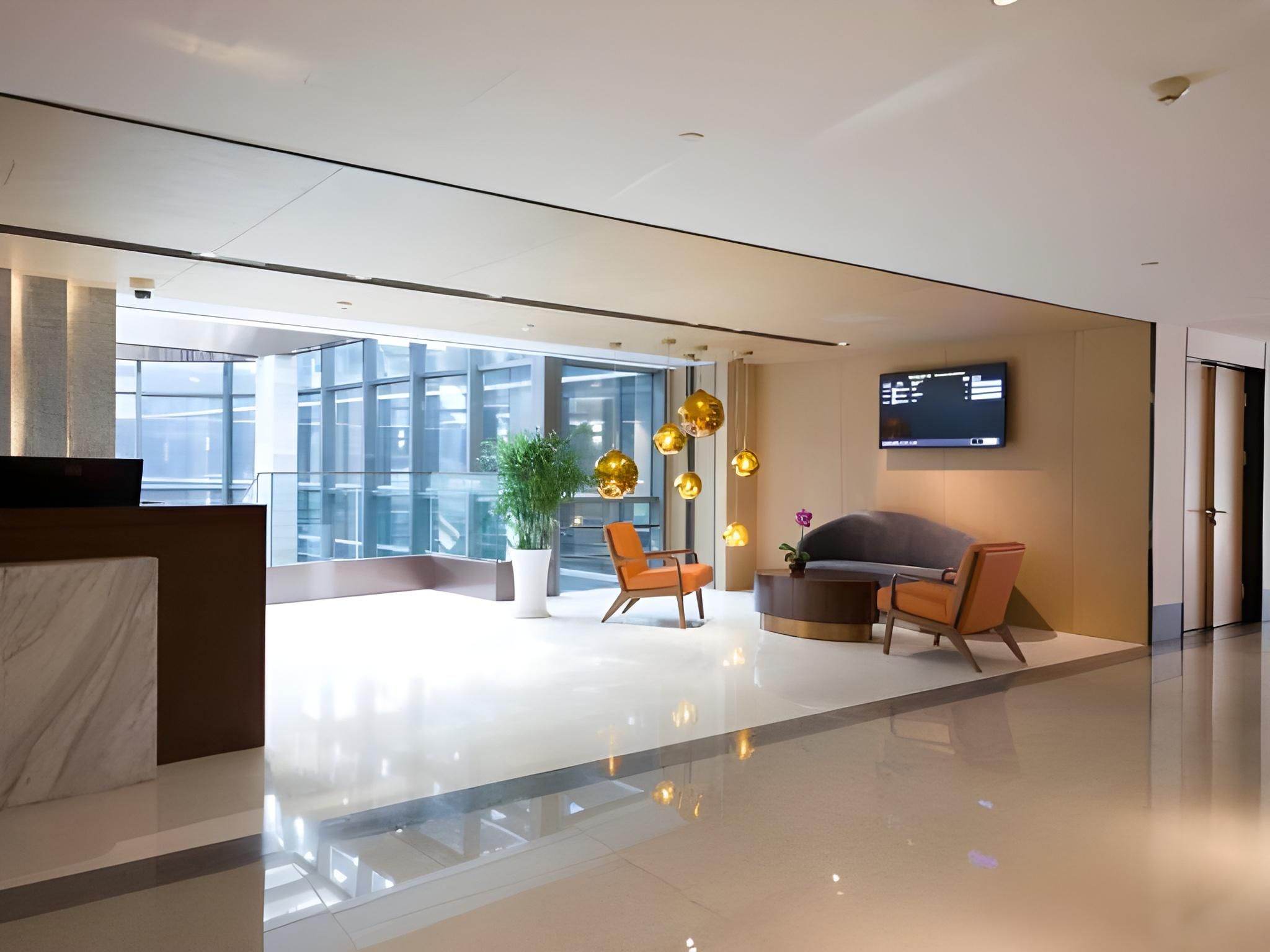 A modern lobby with a reception desk, seating area, and a large window offering a view of the city.
