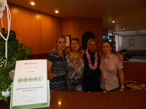 Un grupo de personas en el vestíbulo de un hotel, con una mesa de recepción y un certificado en el mostrador.