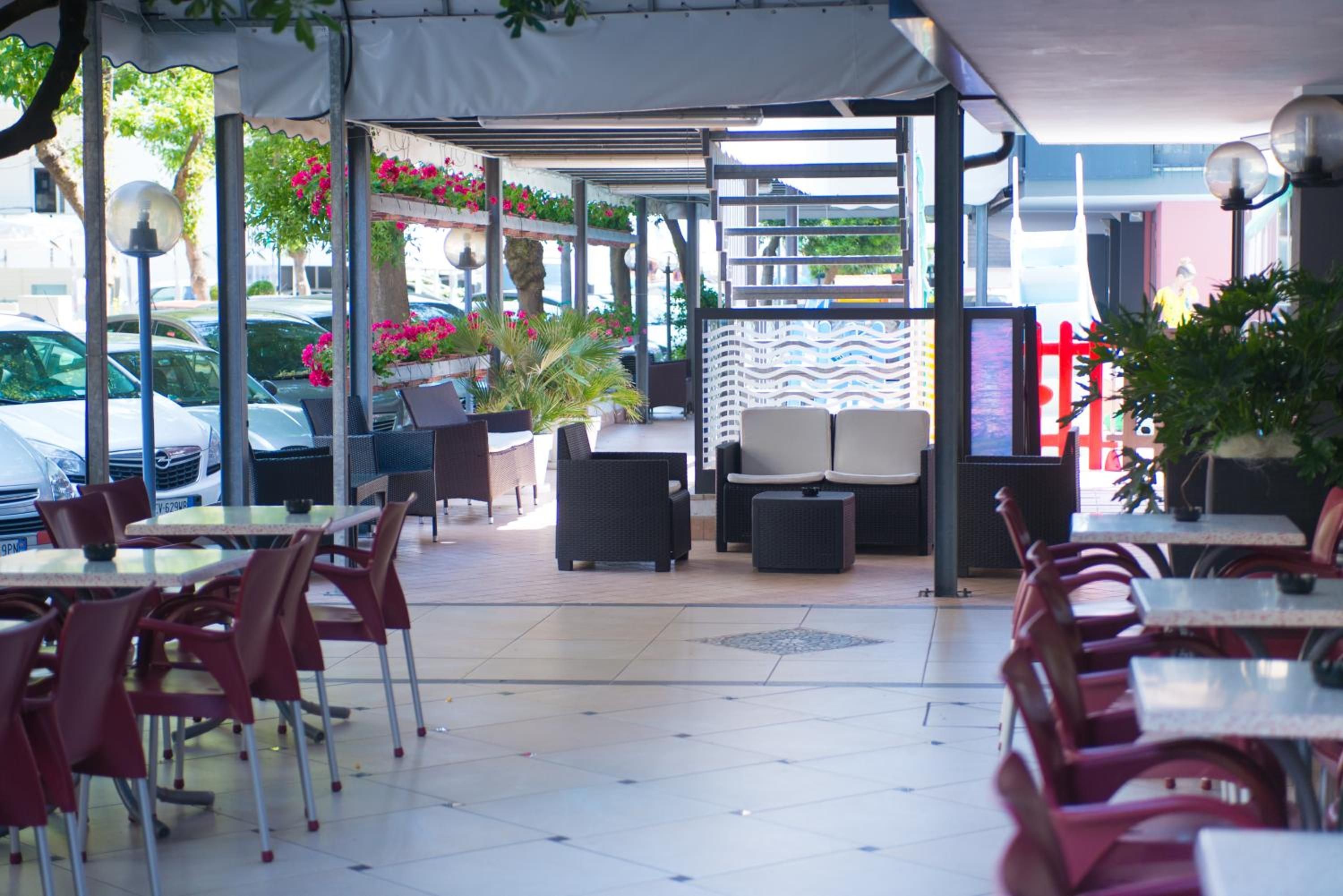 Ein Straßencafé mit Tischen, Stühlen und einer überdachten Sitzgelegenheit, dekoriert mit Topfpflanzen.
