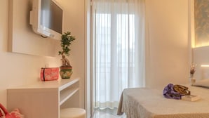 Una habitación de hotel con cama, televisor montado en la pared, una mesita con una planta y una ventana con cortinas.