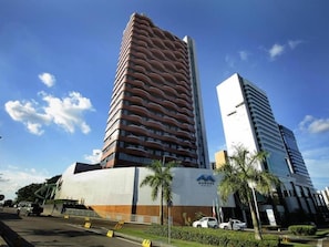 Un edificio moderno con una fachada curva distintiva, un logotipo destacado y un estacionamiento con varios autos.