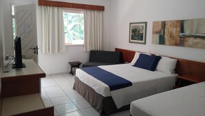 Una camera d'albergo con un letto, una scrivania, una sedia, una TV e una finestra con tende.