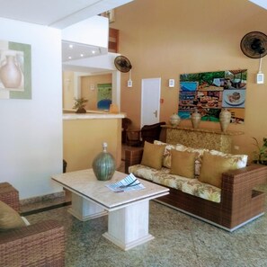 A lobby with a reception desk, a sofa, a coffee table, and a wall with framed pictures. - Riviera Service- Hotel Suites 209 e 308 (Bertioga)