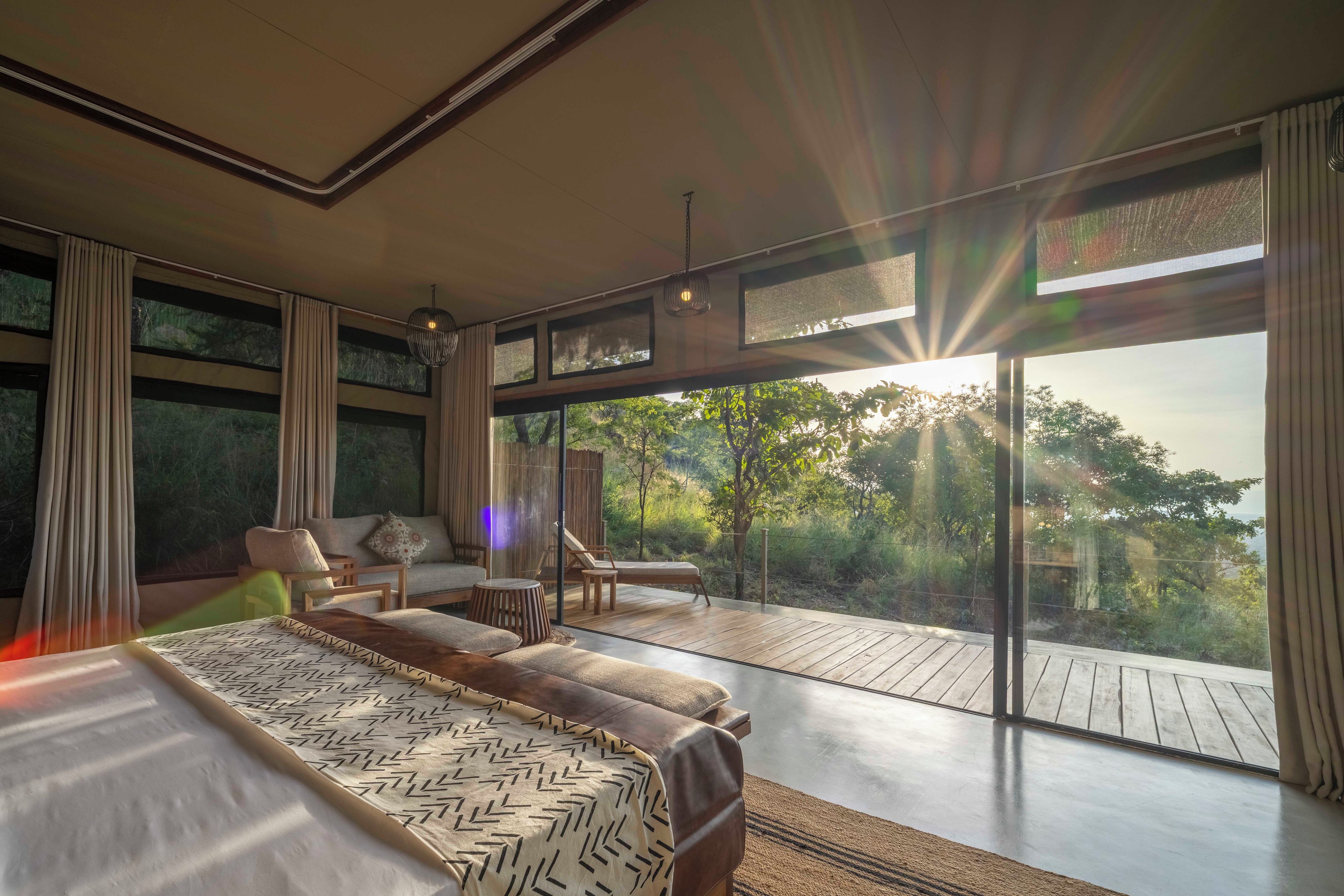 Une chambre moderne avec un grand lit, un canapé et un balcon donnant sur la verdure.