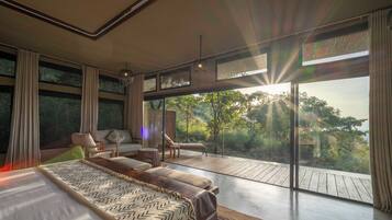 Une chambre moderne avec un grand lit, un canapé et un balcon donnant sur la verdure.