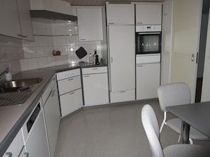 Une cuisine compacte avec des meubles blancs, un four encastré, un évier et un coin repas comprenant une table et des chaises.