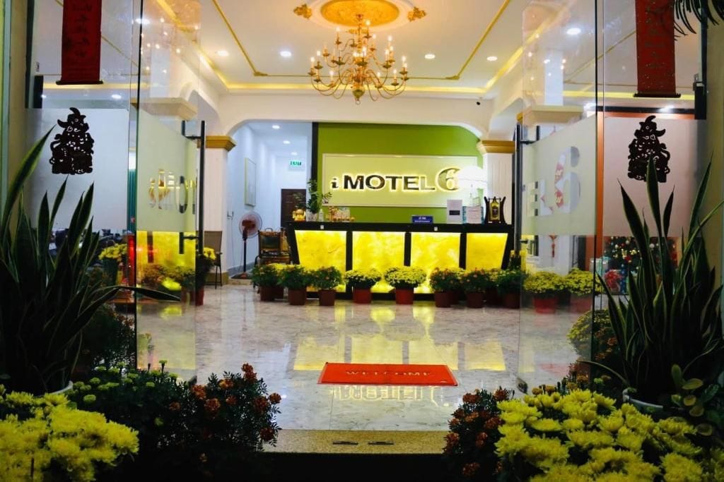 A hotel lobby with a reception desk, a chandelier, and potted plants.