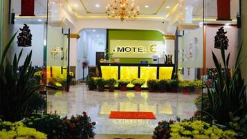 A hotel lobby with a reception desk, a chandelier, and potted plants.