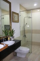 Un baño moderno con cabina de ducha de vidrio, inodoro blanco y encimera negra con lavabo y planta en maceta.