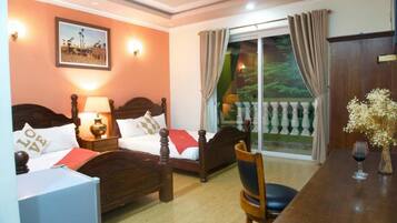 A hotel room with two beds, a dining table, and a view of a balcony with curtains.