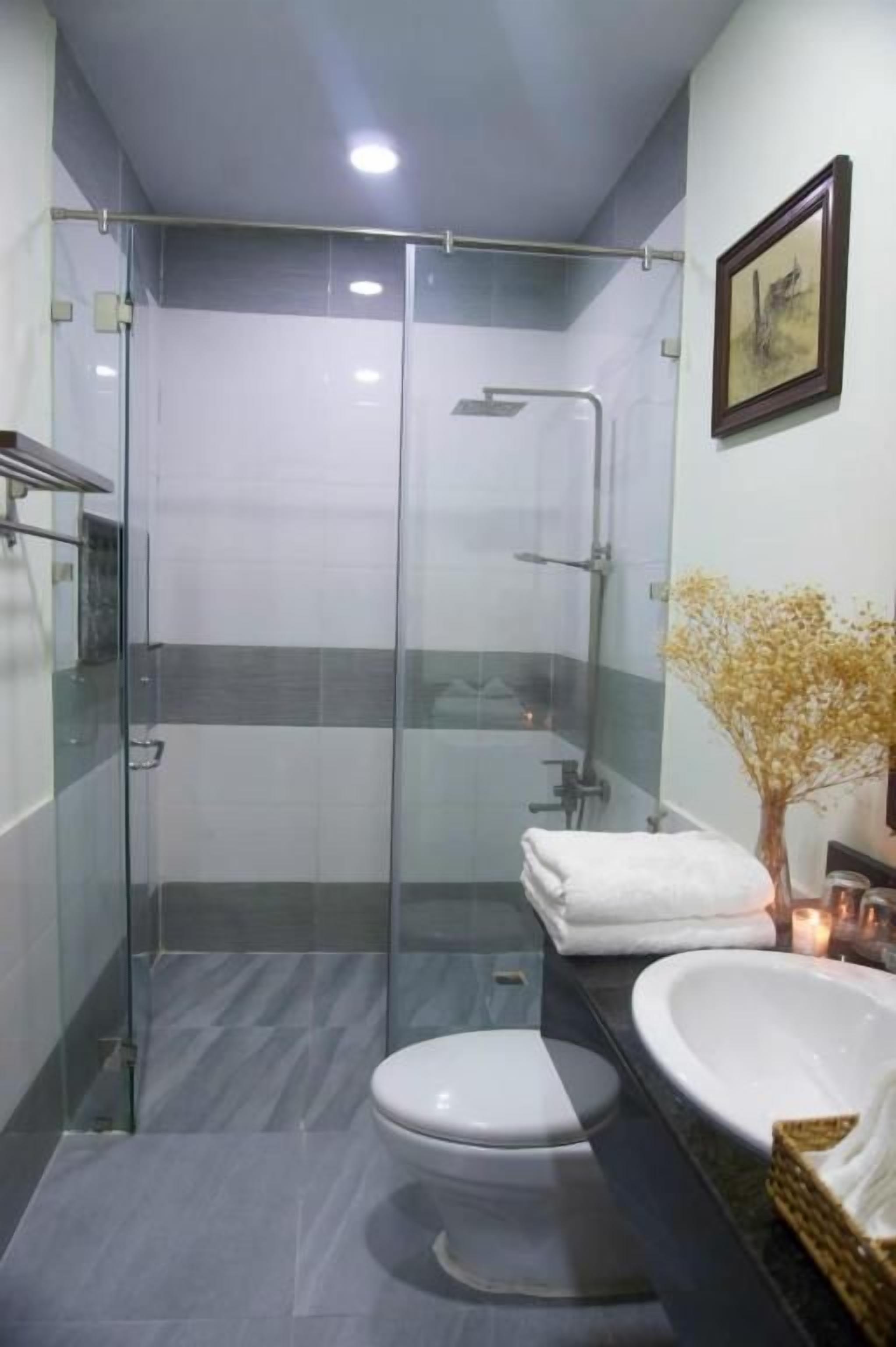 A modern bathroom with a glass-enclosed shower, a white toilet, and a sink with a vase of dried flowers.
