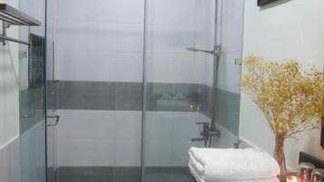 A modern bathroom with a glass-enclosed shower, a white toilet, and a sink with a vase of dried flowers.