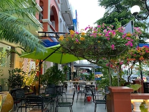An outdoor seating area with tables and chairs, surrounded by greenery and flowering plants.