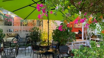 Un espace de détente intérieur avec des tables et des chaises, entouré de plantes en pot et agrémenté d’un parasol vert.