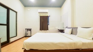 Ein Hotelzimmer mit Bett, einem kleinen Tisch, einem Stuhl, einer Klimaanlage und einem Fenster mit Vorhängen.