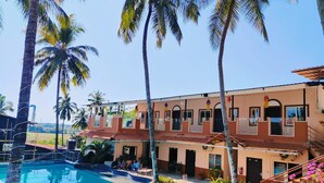 Ein Hotel mit Schwimmbad, Palmen und einem zweistöckigen Gebäude mit Balkonen.