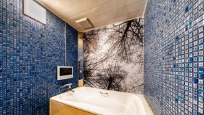 A bathroom with a bathtub, blue mosaic walls, and a tree branch mural. - Hotel Luna Modern Sakuranomiya (Osaka)