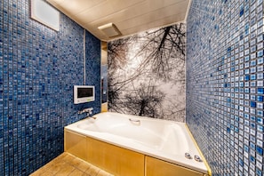 Ein Badezimmer mit Badewanne, blauen Mosaikwänden und einer Wandmalerei mit einem Ast.