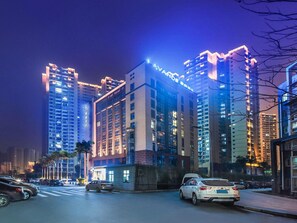 A high-rise building with illuminated signage, a street with parked cars, and surrounding taller buildings. - Lifeng Hotel (Chongqing)