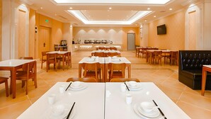 A spacious dining area with multiple tables and chairs, a coffee station, and a television mounted on the wall. - Vienna International Hotel (Foshan)