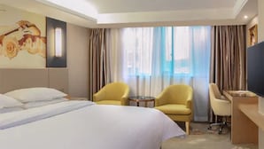 Een hotelkamer met een groot bed, twee fauteuils, een bureau en een televisie.