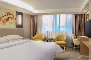 Habitación de hotel con una cama grande, dos sillones, un escritorio y un televisor.