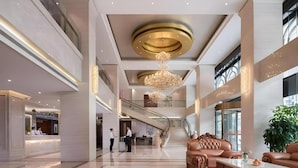 Een ruime lobby met een centrale trap, een receptiebalie en een zithoek met een kroonluchter.