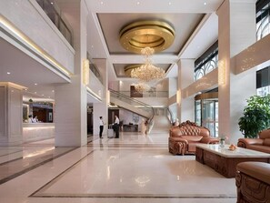 Un vestíbulo espacioso con una escalera central, una mesa de recepción y un área de estar con un candelabro.