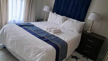 Et hotelværelse med seng, to sengeborde, lamper og et vindue med gardiner.