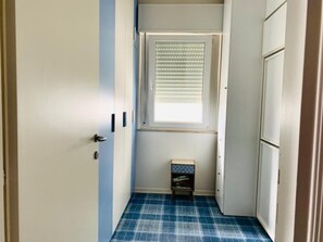A narrow hallway with a door on the left, a window with blinds, and a small cabinet on the right. - Seafront apartment by the city centre (Lignano Sabbiadoro)