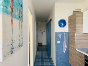 Een gang met een blauw geruit vloerkleed, een klok aan de muur en een deur aan het einde.