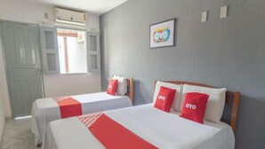 Habitación de hotel con dos camas, cada una con cubrecama rojo y blanco, cabeceros de madera y una ventana con contraventanas.