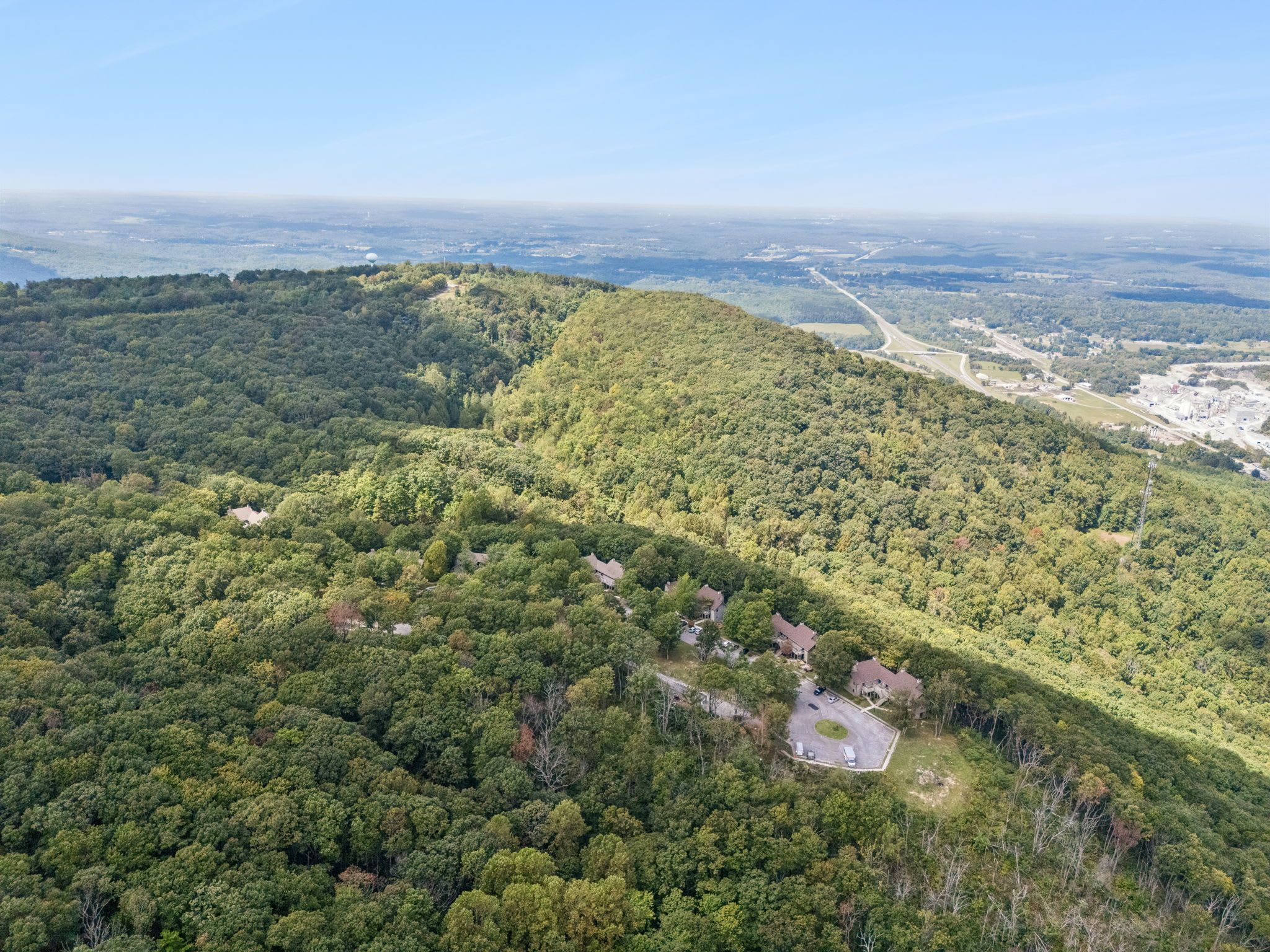 Un quartier résidentiel où les maisons sont entourées d’une forêt dense, sous un ciel dégagé, et où l’on aperçoit une route au loin.