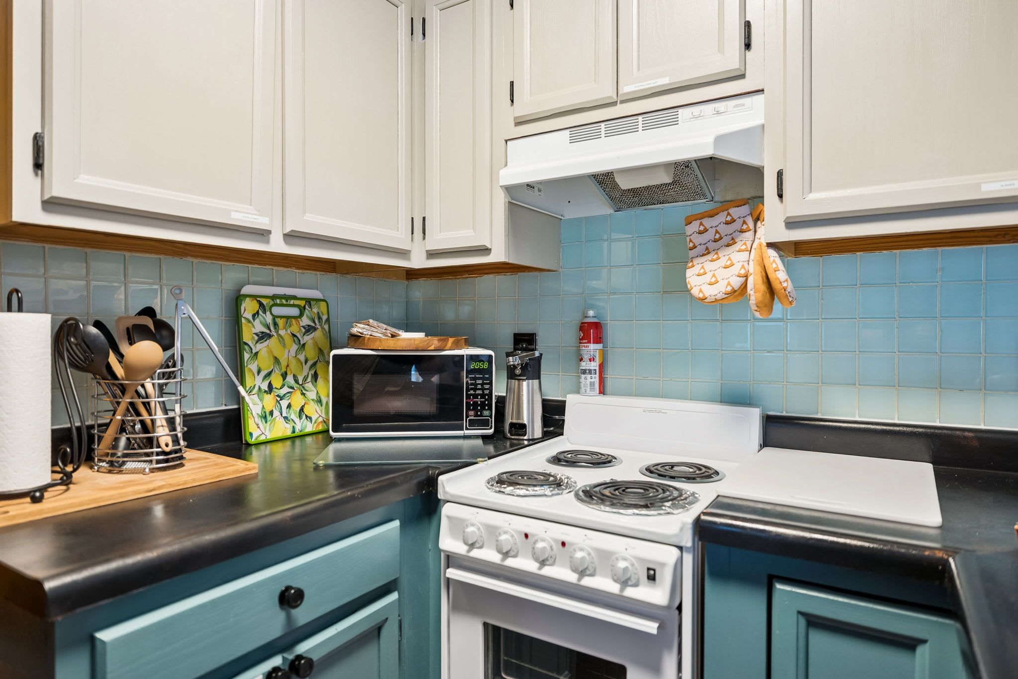 A kitchen with white cabinets, a stove, a microwave, and a coffee maker.