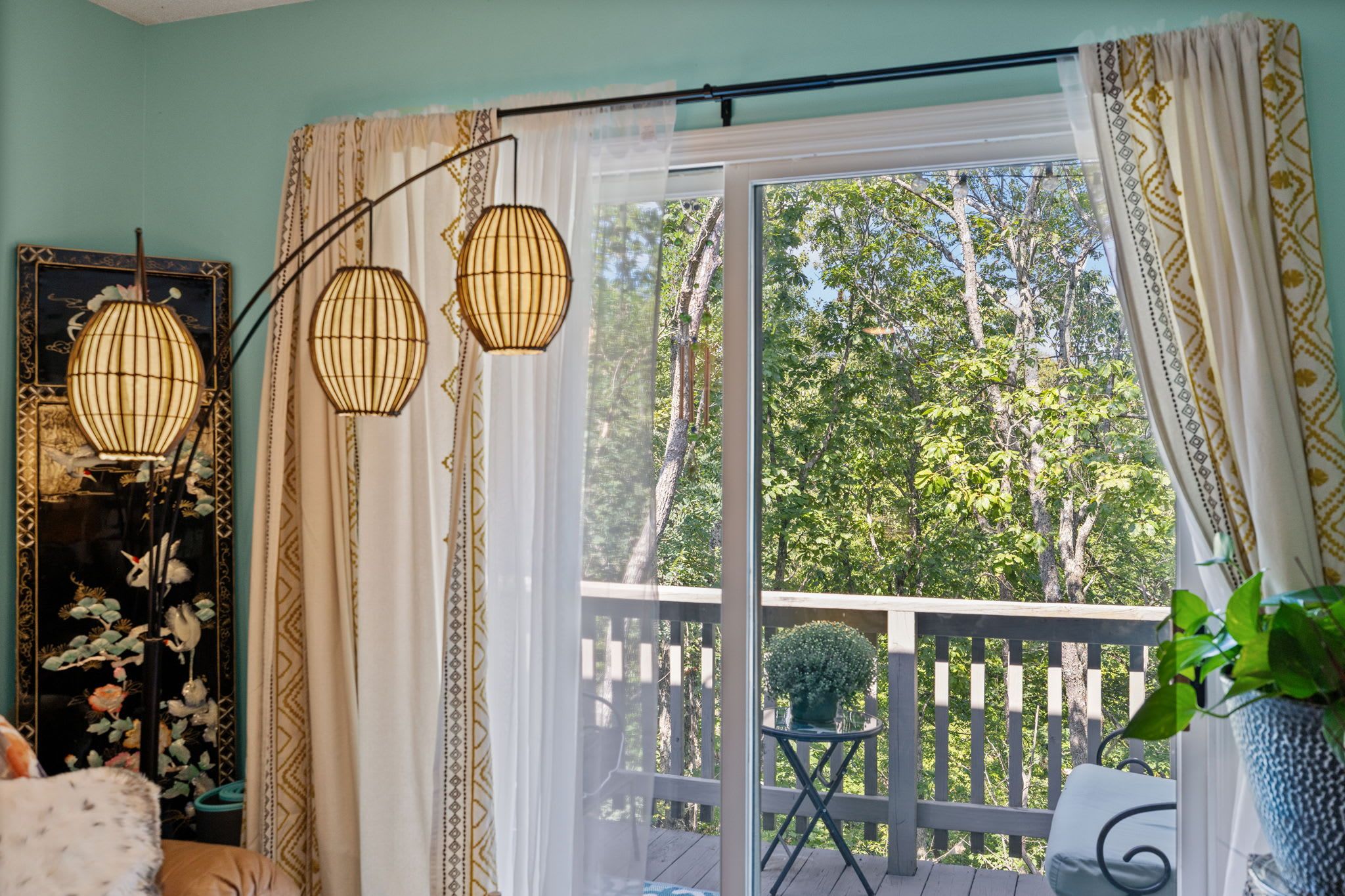 A room with a large sliding glass door leading to a deck, a decorative lamp, and a framed artwork.