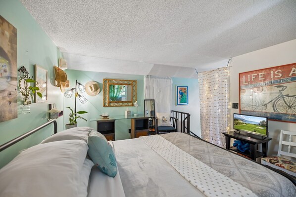 Un dormitorio con cama, escritorio, silla, televisor y varias decoraciones en la pared.