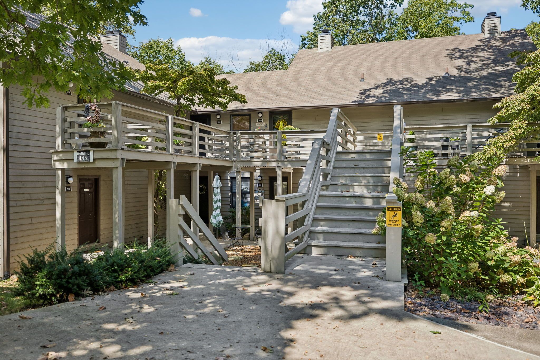 A building with a covered outdoor area, a staircase, and a caution sign for slippery surfaces.