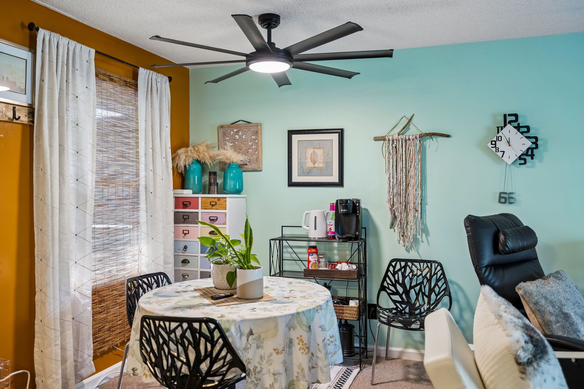 Un coin repas comprenant une table ronde, des chaises, un ventilateur de plafond et une horloge murale.
