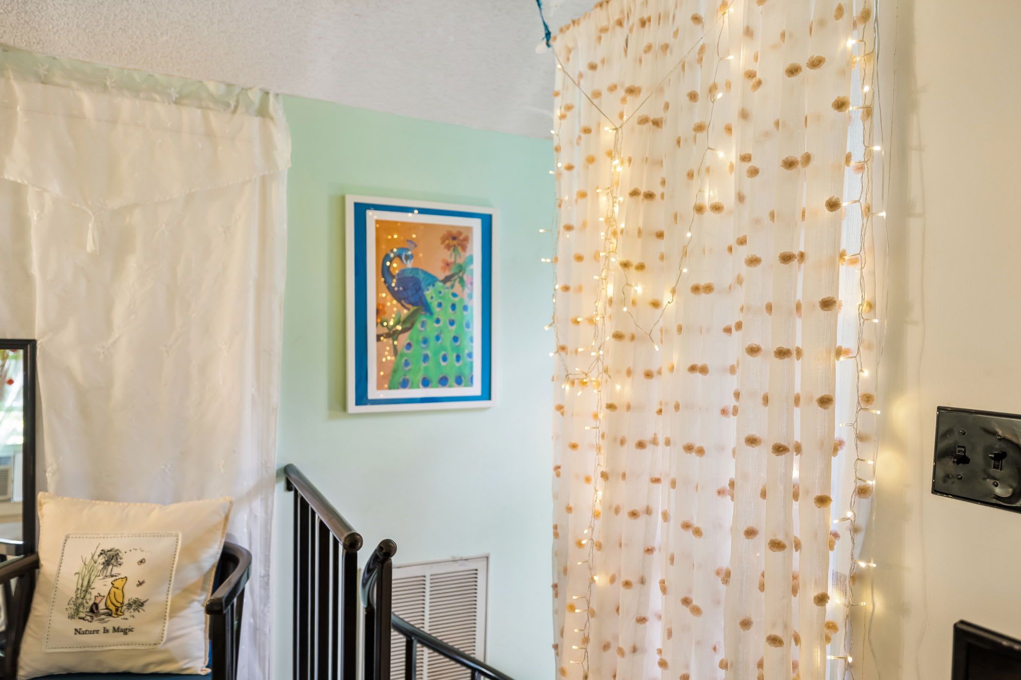 A room with a bed, a pillow with a nature-themed design, a framed picture on the wall, and a curtain with a floral pattern.