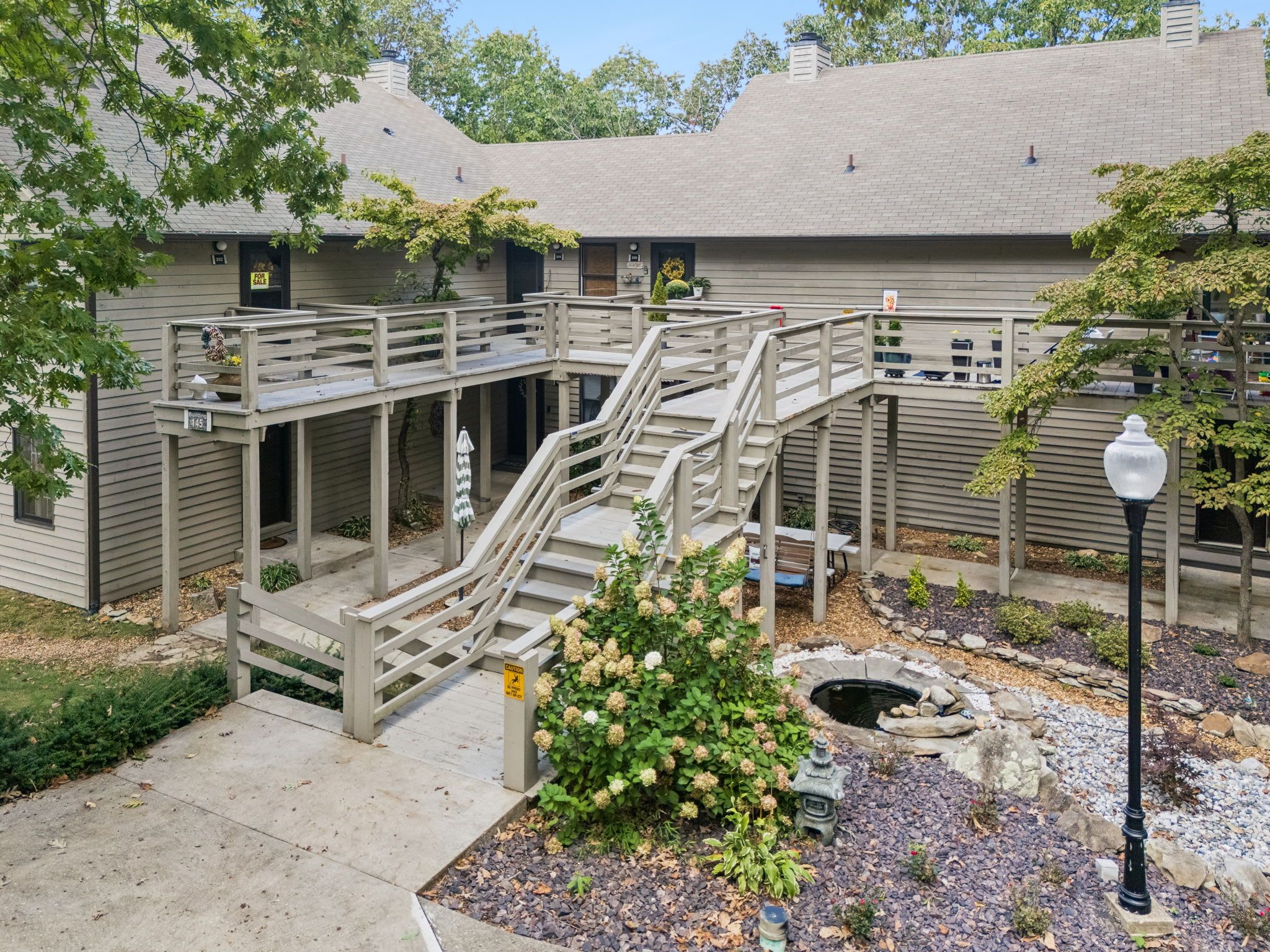 A multi-level outdoor deck with stairs connecting different levels, surrounded by greenery and a small pond.