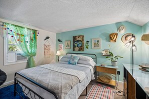 A bedroom with a bed, a desk, a chair, and a window with curtains.