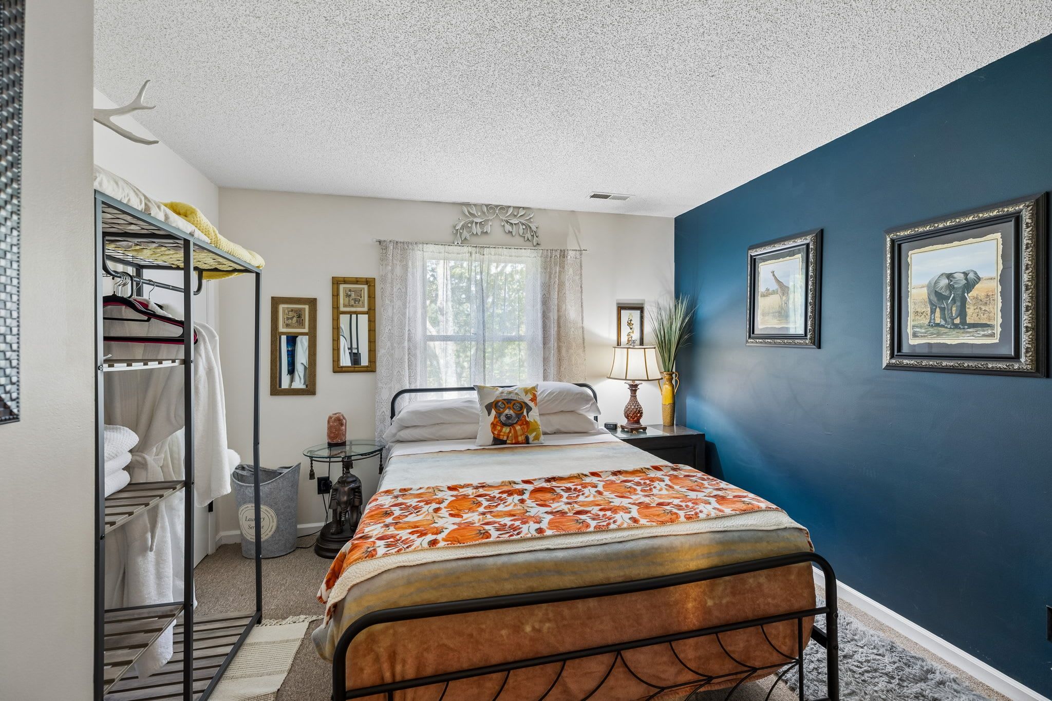 A bedroom with a bed, a wardrobe, a mirror, a window with curtains, and wall-mounted pictures.