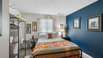 A bedroom with a bed, a wardrobe, a mirror, a window with curtains, and wall-mounted pictures.