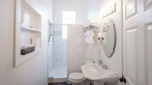 A compact bathroom with a white sink, toilet, and shower area. There is a window providing natural light and a towel rack with folded towels. - Relaxing Apt near Cherokee Park and Frankfort Ave! (Louisville)