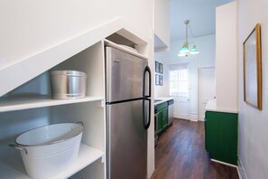 A kitchen with a stainless steel refrigerator, a white pot on a shelf, and a green cabinet.