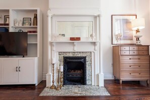 A living room with a fireplace, a television, a cabinet with decorative items, and a dresser.